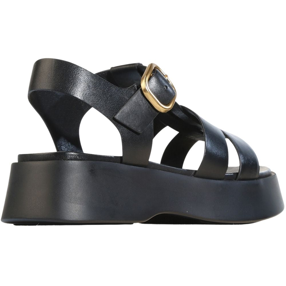 A black platform sandal with multiple leather straps and a prominent gold-tone buckle, shown from a side profile view on a white background.