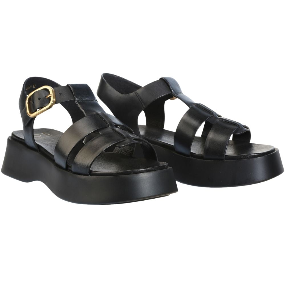 A pair of black leather platform sandals with wide T-bar straps, a rear ankle strap with a gold-tone buckle, and chunky black soles, shown on a plain white background.