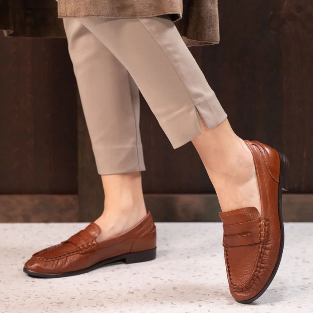 Brown leather loafers worn with beige pants on a neutral background