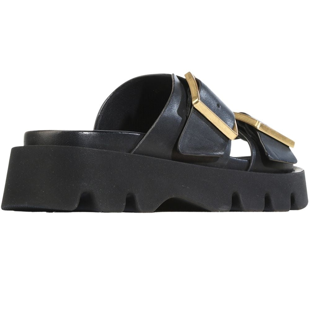 A single black leather platform slide sandal with a chunky lug sole and a prominent gold-tone metal buckle detail on the strap, shown from a side profile view against a plain white background.