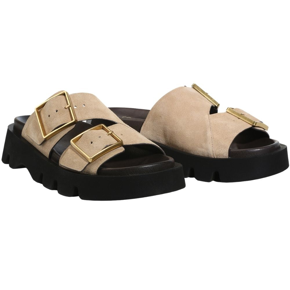 A pair of beige double-strap slide suede leather sandals with chunky gold-tone buckles and a thick black lug sole, shown in a side profile on a white background.