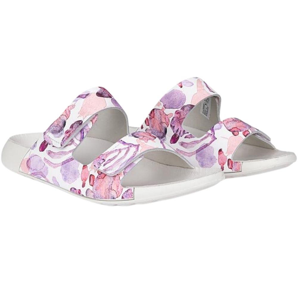 A pair of women's slide sandals with a white base and a pink and purple watercolor floral pattern on the straps, shown against a plain white background.