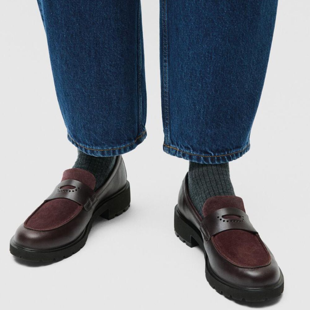 Brown loafers worn with blue jeans on a light gray background