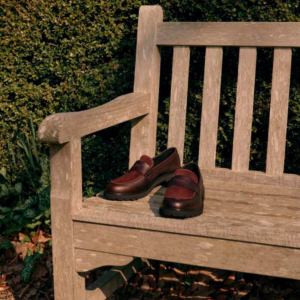 Pair of brown loafers on a wooden bench with a garden background
