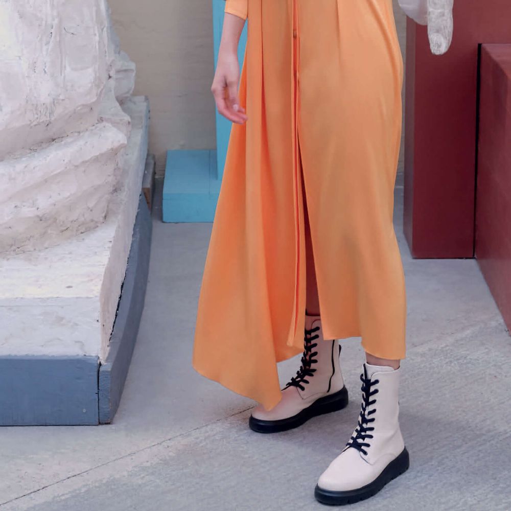 Person wearing an orange dress and white boots with black soles on a city street.