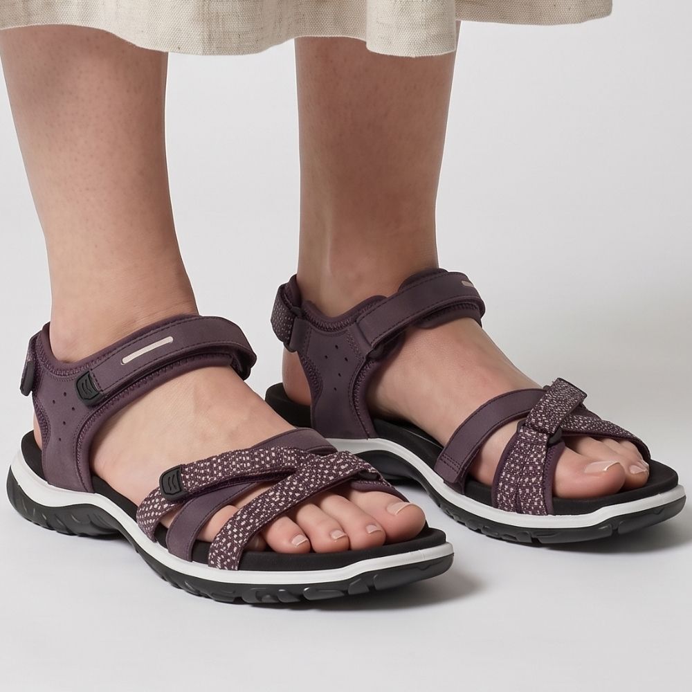 Lady wearing a linen skirt with a pair of ECCO OFFROAD ROAM sandals with merlot coloured straps and a black sole, against a grey studio background.