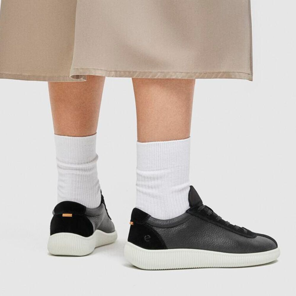 Person wearing black sneakers with white socks on a plain background