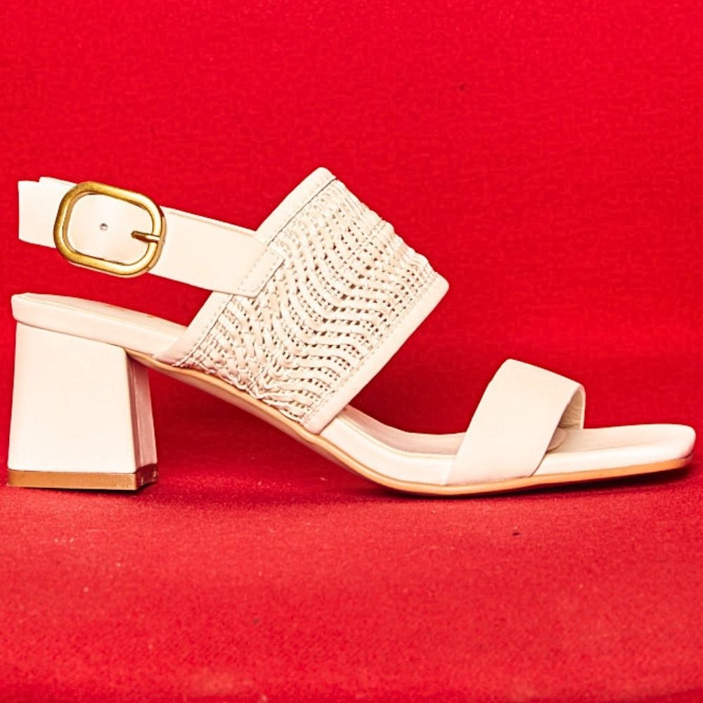 A single women's heeled sandal in white leather with a textured woven upper strap, a square block heel, and a gold buckle ankle strap, set against a solid red background.