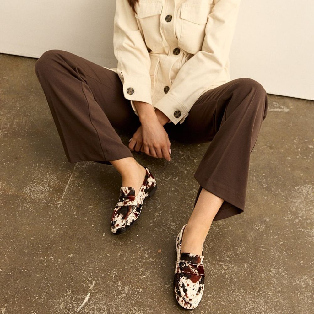 Person wearing animal print patterned loafers sitting on a concrete floor.