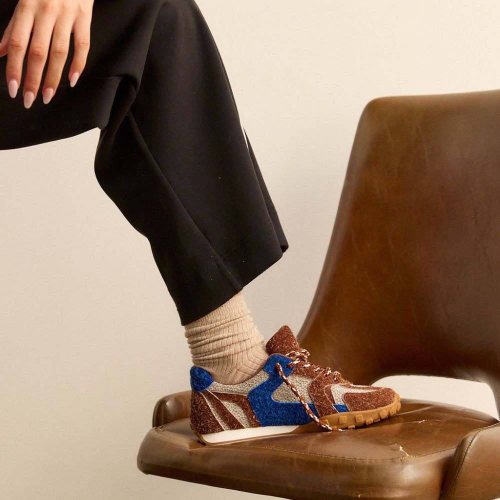 Person wearing brown and blue sneakers with beige socks, sitting on a brown chair.