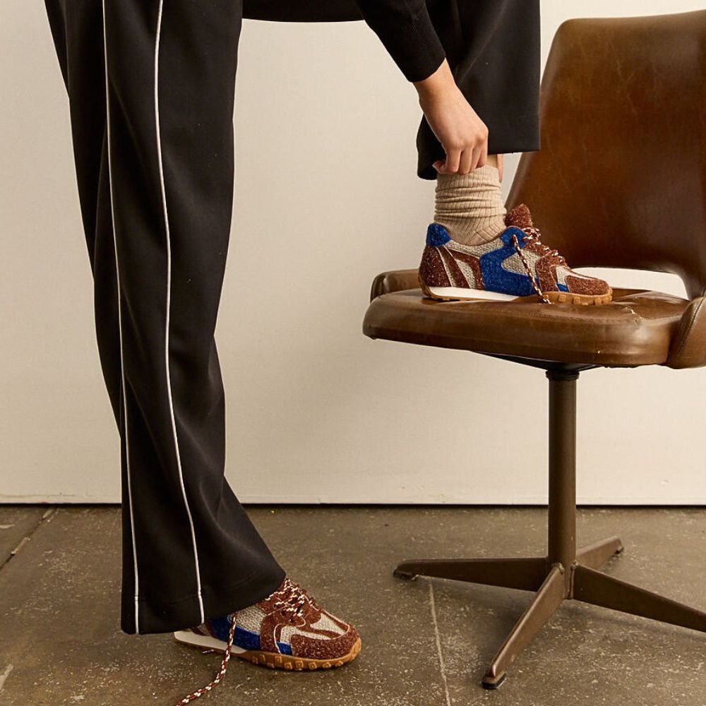 Person wearing brown shoes with blue accents, standing on a chair.