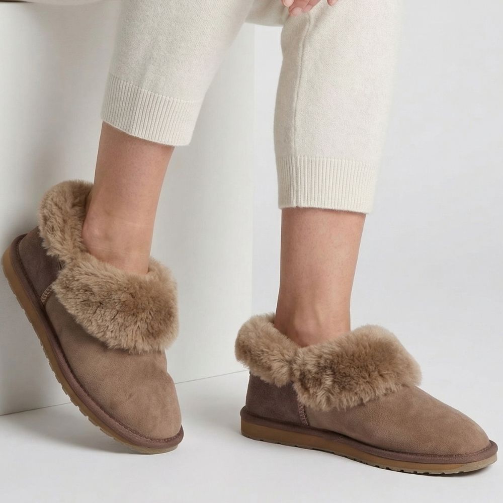 Brown suede slippers with fur wool trim worn by a person on a white background