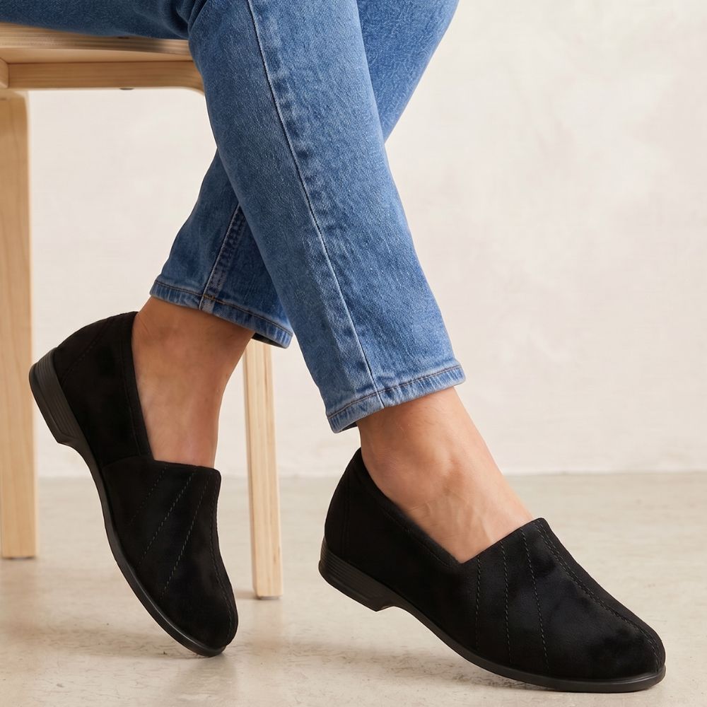 Person wearing black slippers and blue jeans sitting on a wooden chair.