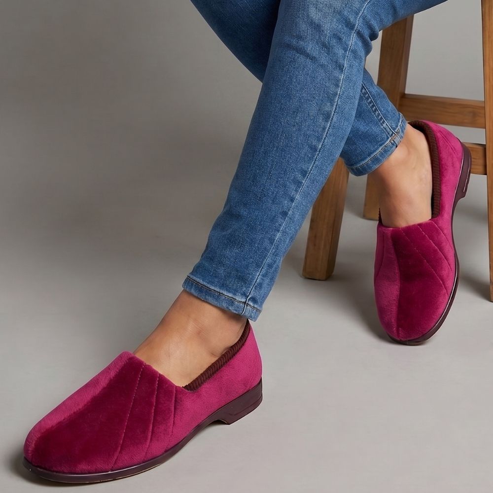 Person wearing burgundy slippers and blue jeans on a gray background