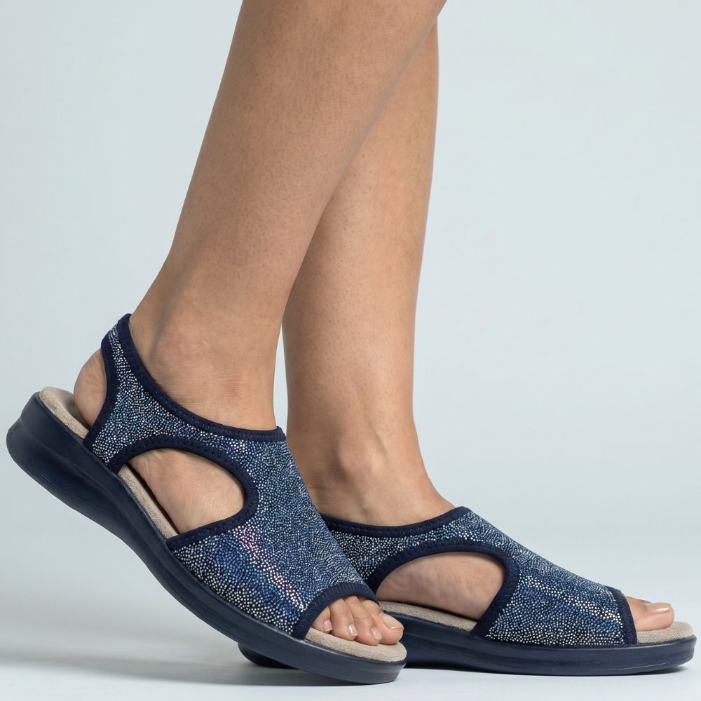 Person wearing black sandals with glittery texture on a white studio background