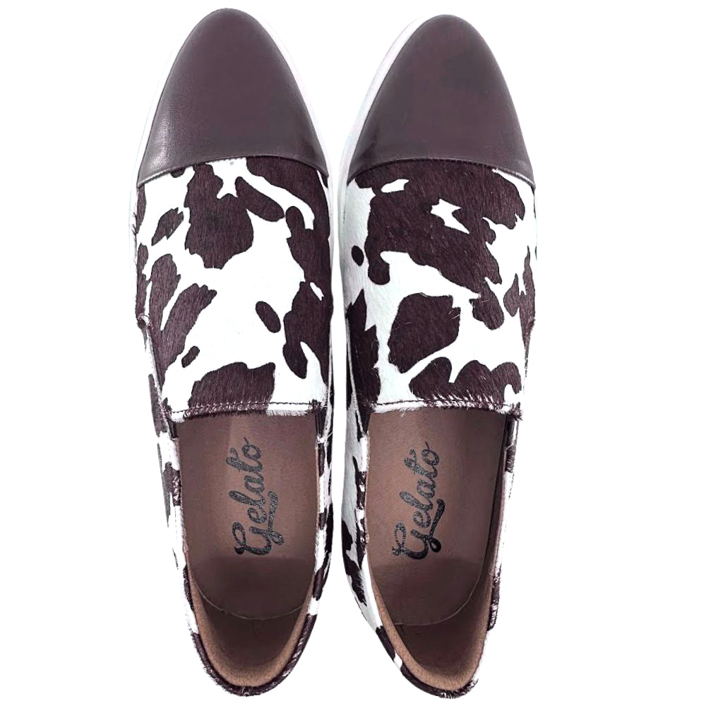 Pair of brown and white loafer sneakers with cow print pattern and brown accents on a white background