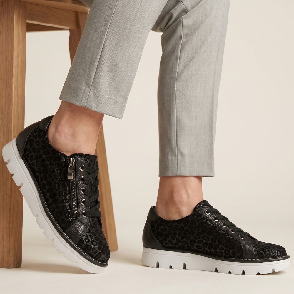 Black leopard print sneakers worn with gray pants on a neutral background