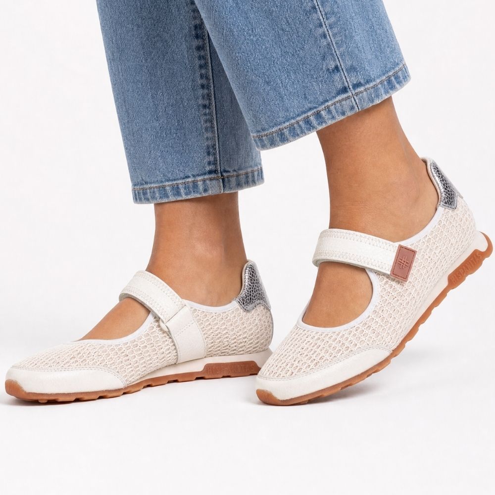 A pair of women's Mary Jane-style shoes worn with light blue jeans. The shoes feature an off-white mesh and leather upper, a Velcro strap with a small brown leather accent, and a brown rubber sole, shown against a plain white background.