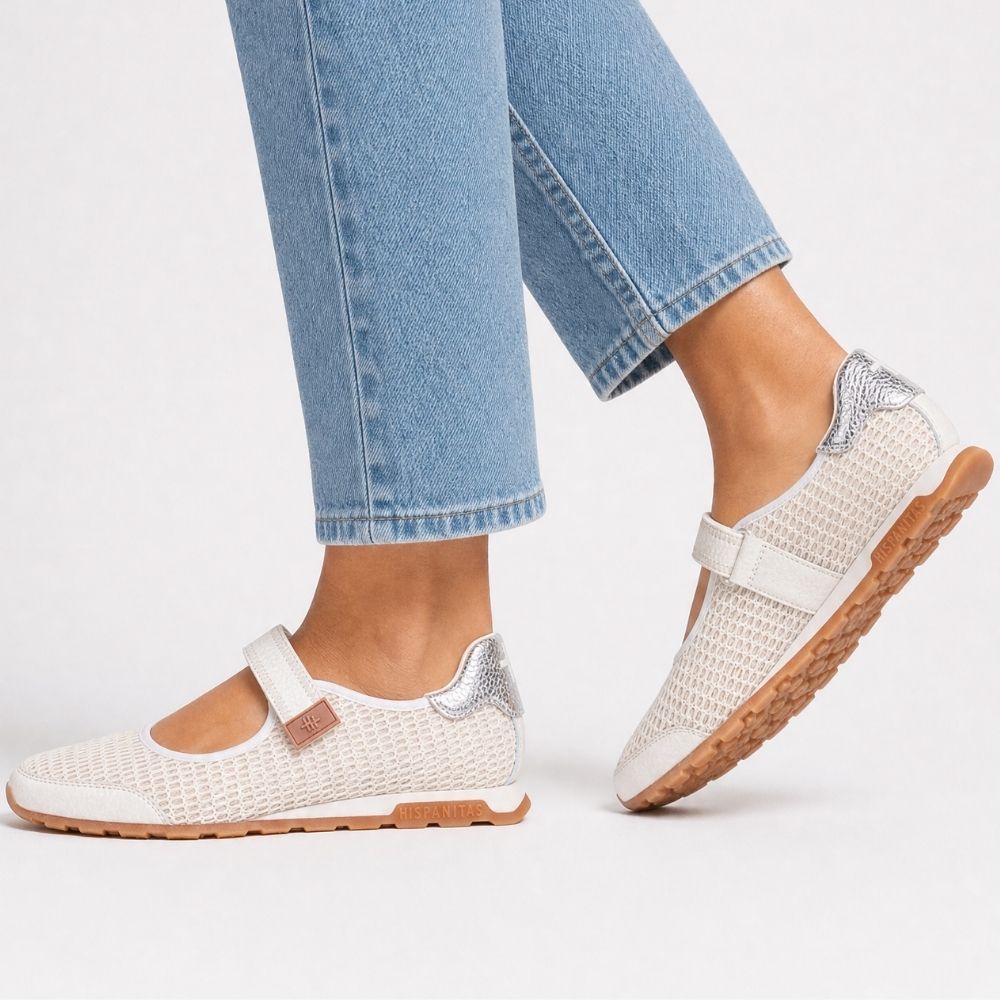 A pair of women's Mary Jane-style shoes worn with light blue jeans. The shoes feature an off-white mesh and leather upper, a Velcro strap with a small brown leather accent, and a brown rubber sole, shown against a plain white background.