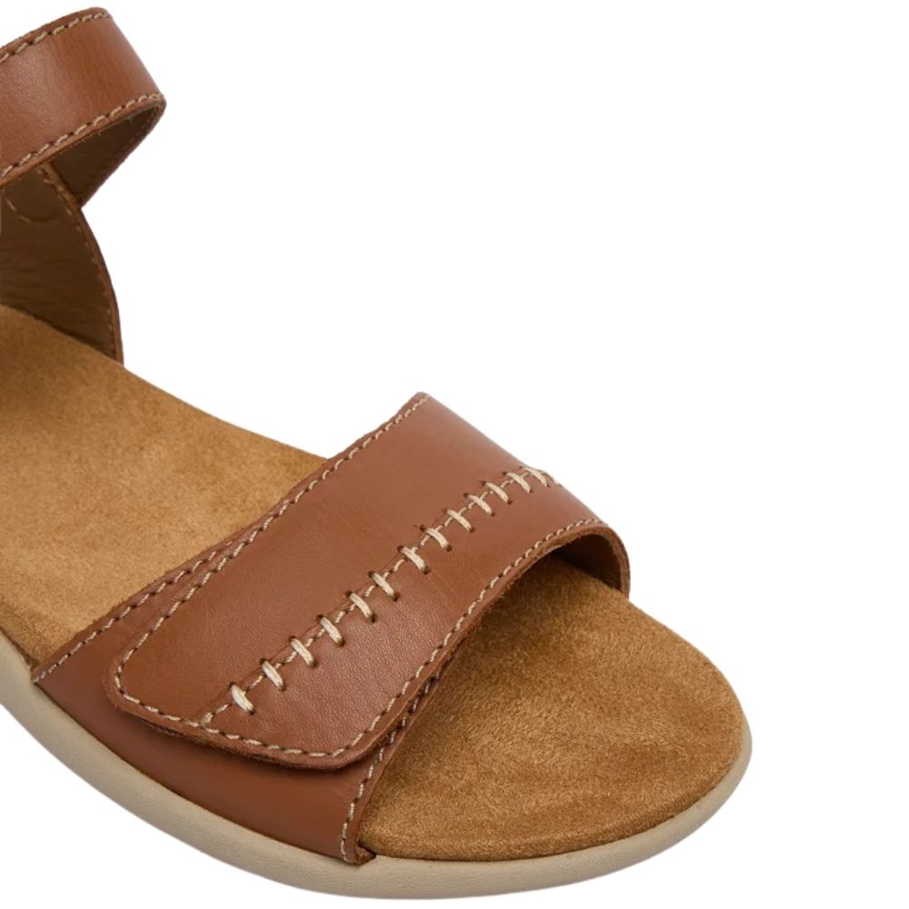 A close-up of a tan leather sandal with a wide strap featuring decorative stitching, a tan footbed, and a light-colored sole, shown on a plain white background.