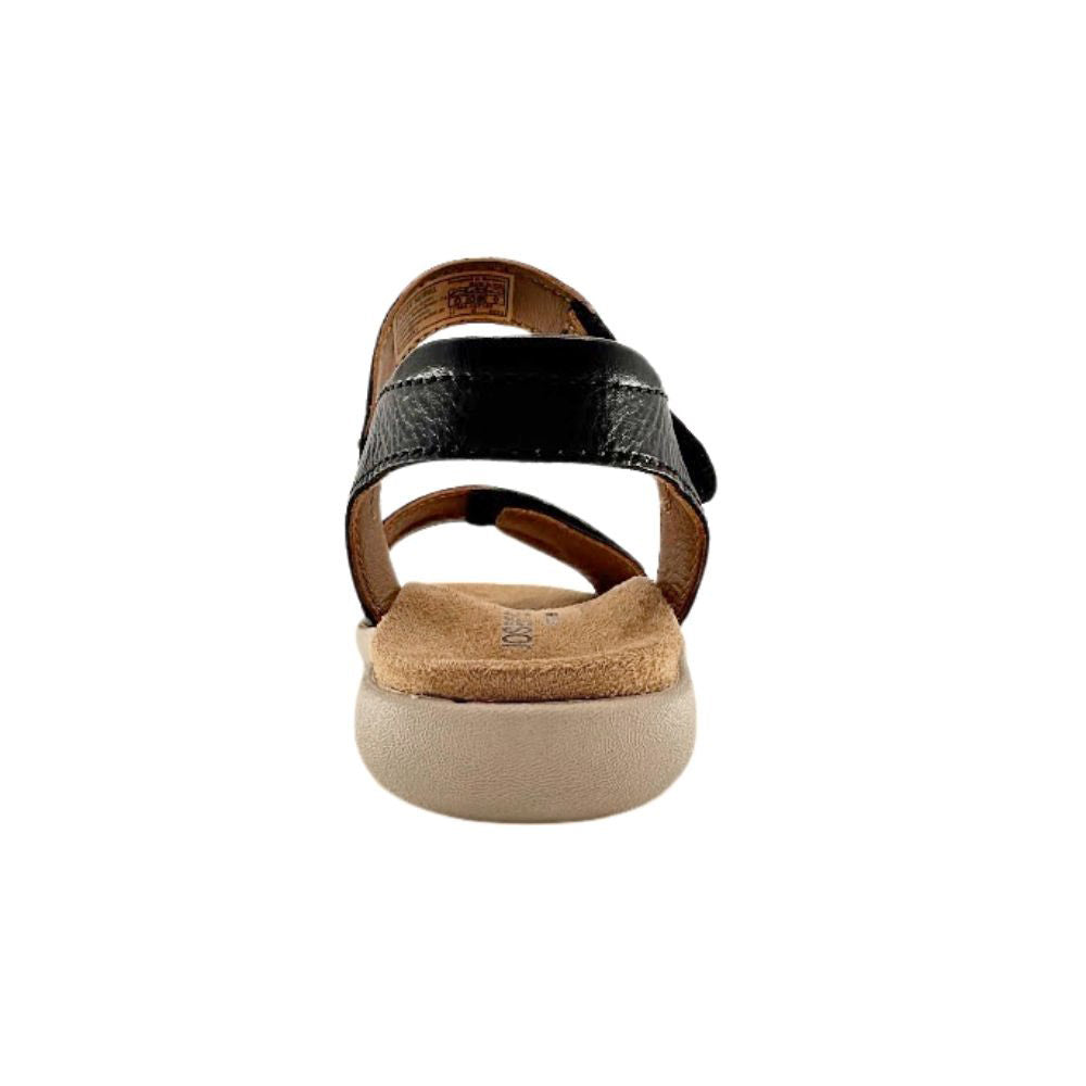 A single women's flat sandal shown from the back, featuring a black leather strap, a tan footbed, and a thick beige sole, set against a plain white background.