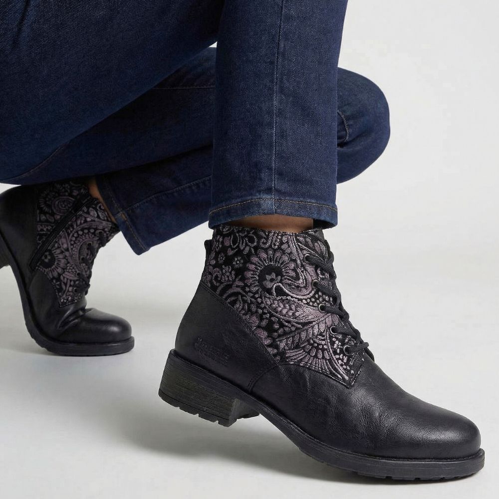 Black boots with intricate patterns worn by a person sitting on a white surface.