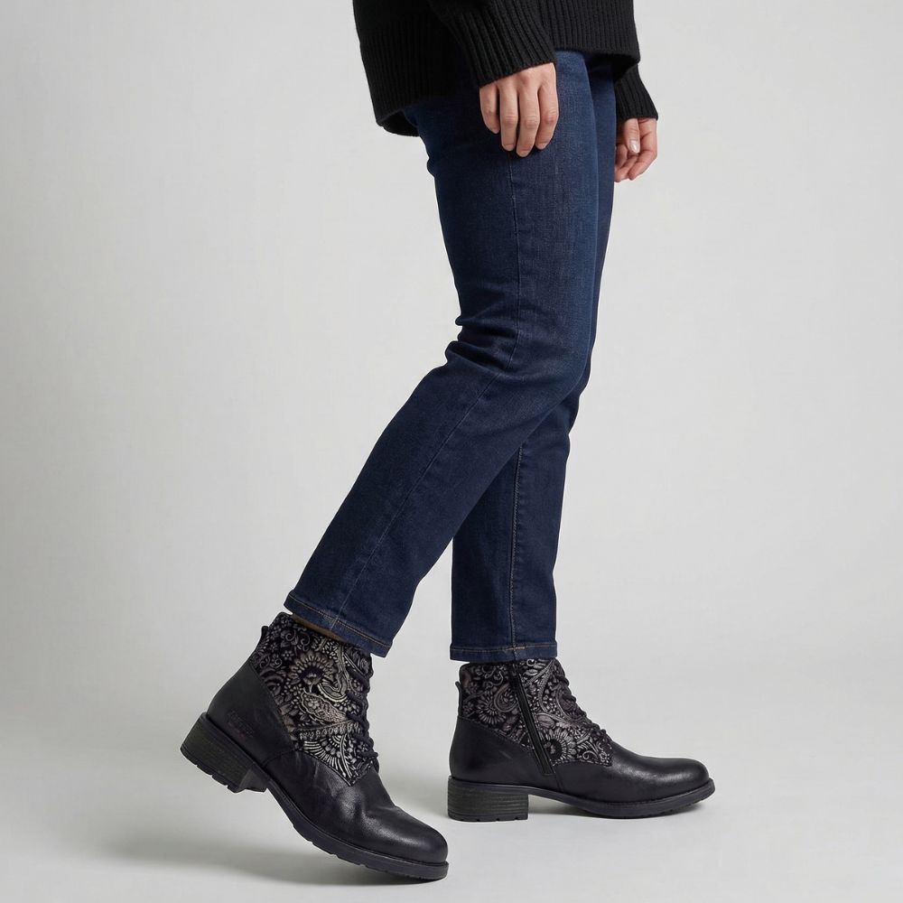 Person wearing black lace-up boots with floral embellishment and blue jeans on a light gray background