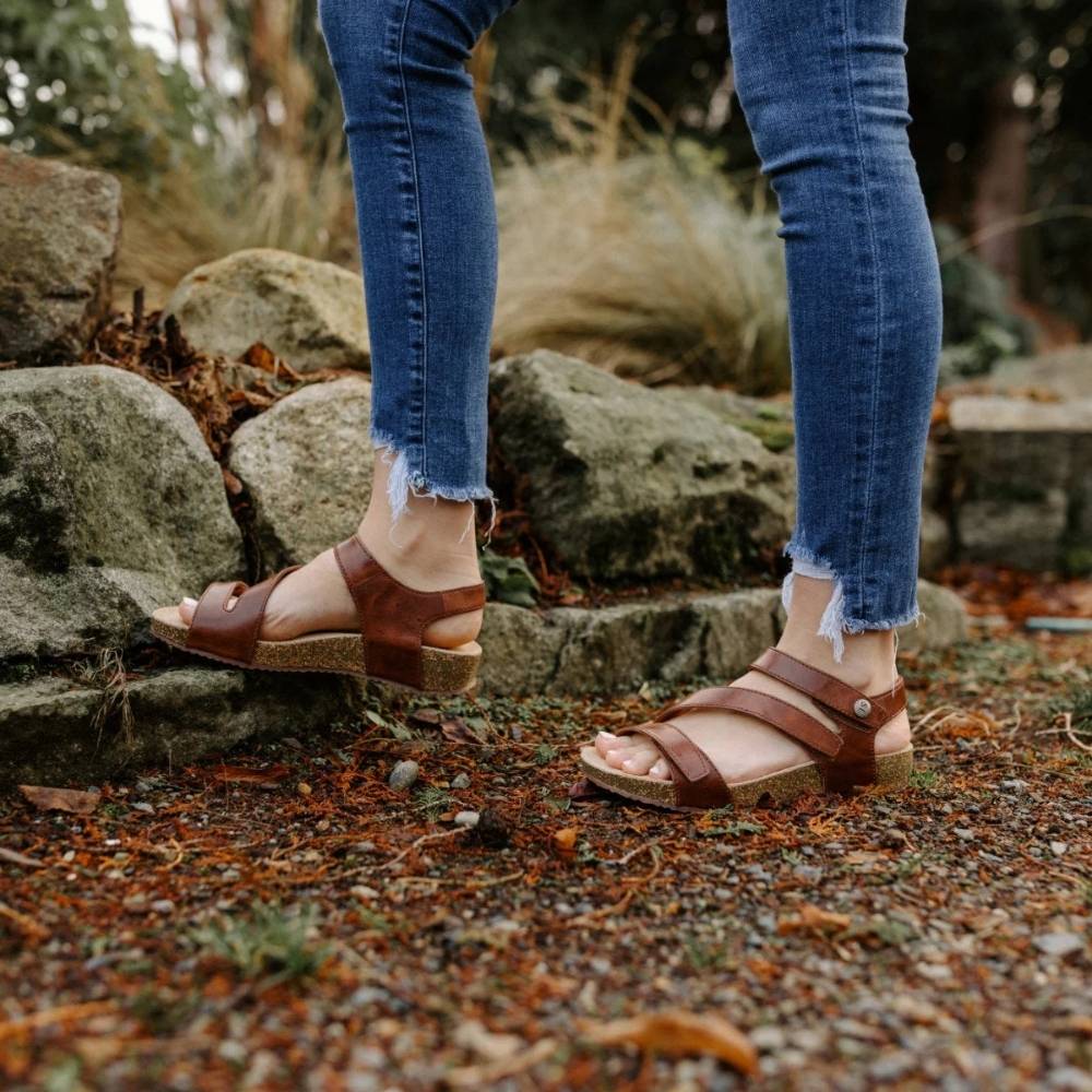Person wearing brown sandals and blue jeans standing on a rocky ground.