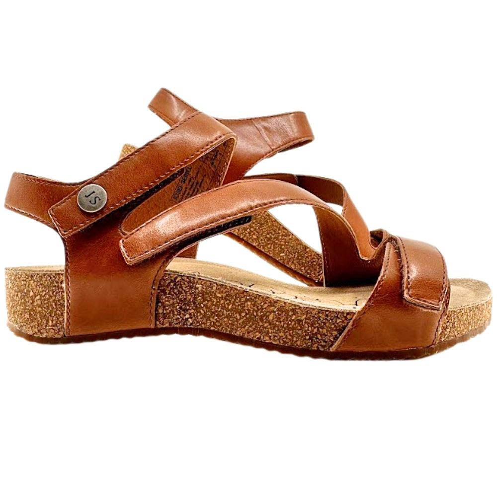 A brown leather strappy sandal with a cork wedge heel and a small silver-tone metal button on the ankle strap, shown from a side profile view against a white background.