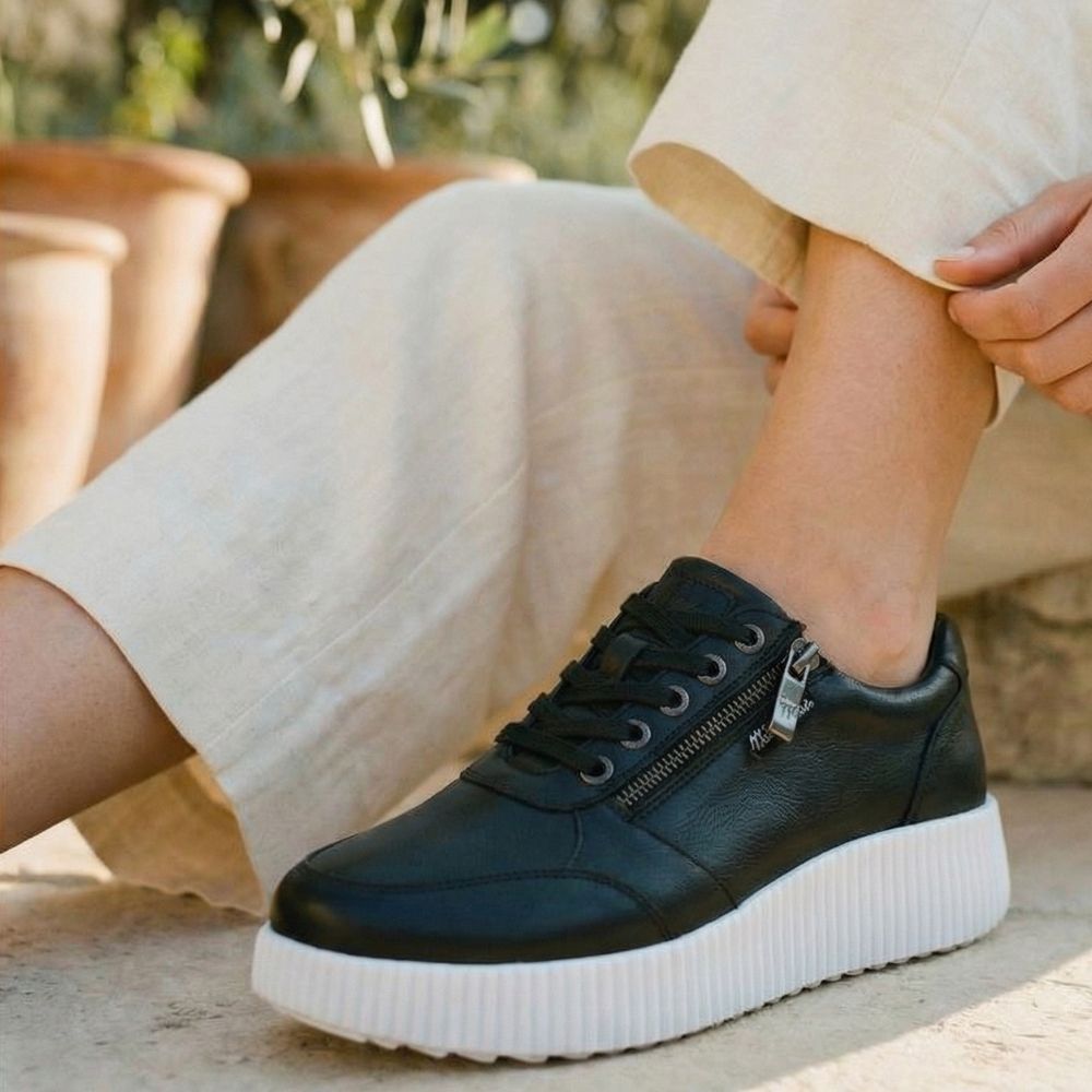 Person wearing a black sneaker with a white sole outdoors.