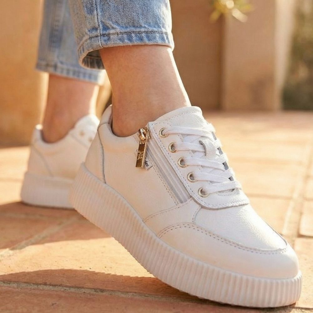 White sneakers with a gold zipper on a blurred outdoor background