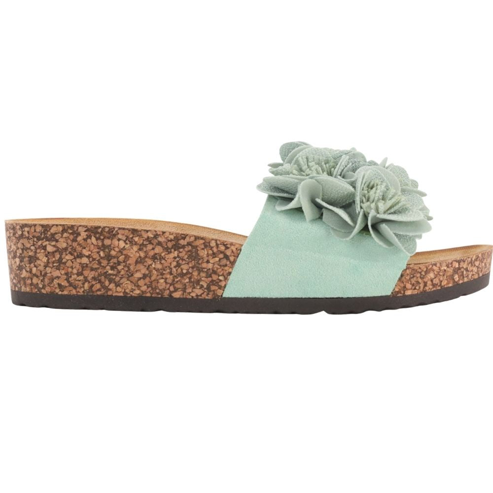 A mint green slide sandal with a wide strap featuring three dimensional fabric flowers, a cork-look wedge heel, and a black outsole, shown against a plain white background.
