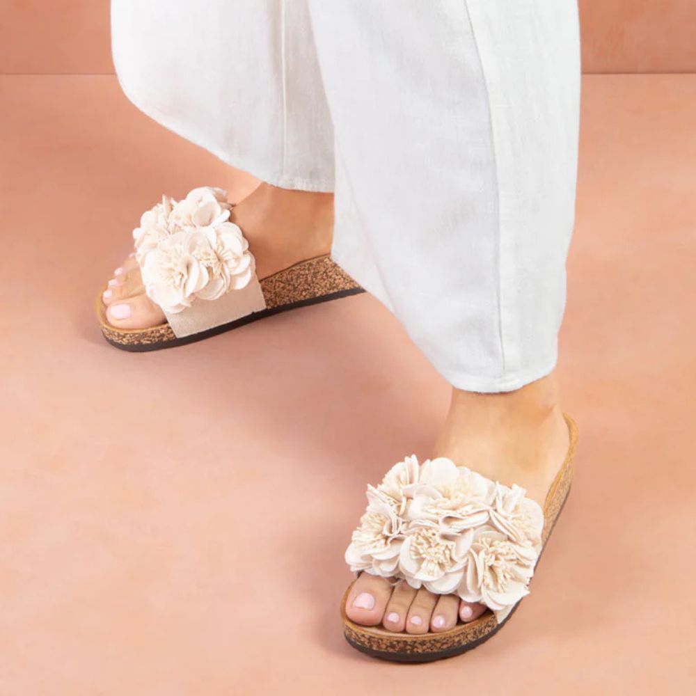Beige floral sandals worn with white pants on a coral background