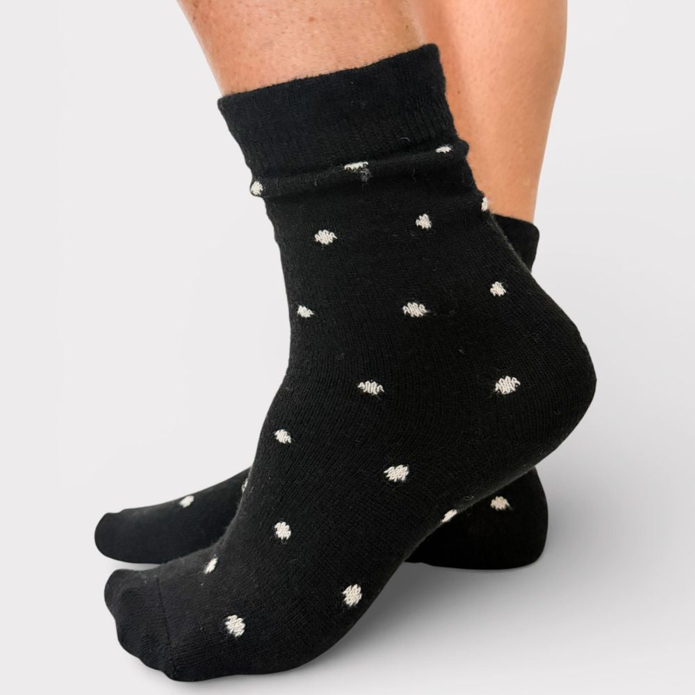 Black socks with white polka dots worn by a person on a light gray background