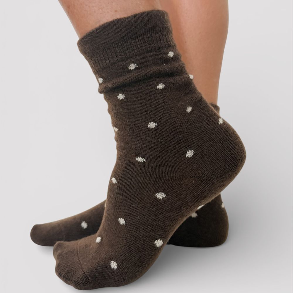 Chocolate brown socks with ivory polka dots worn by a person on a light gray background