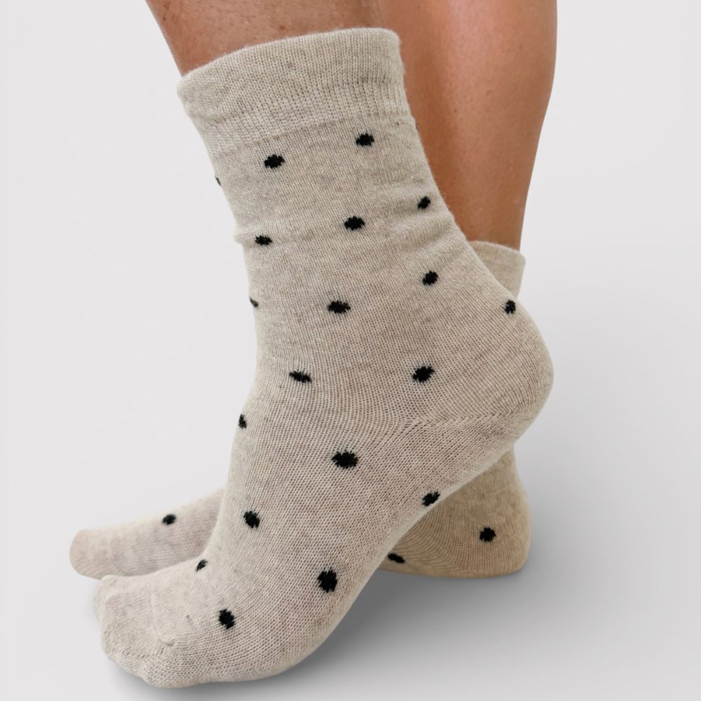 Beige socks with black polka dots and frill cuff worn by a person on a light gray background
