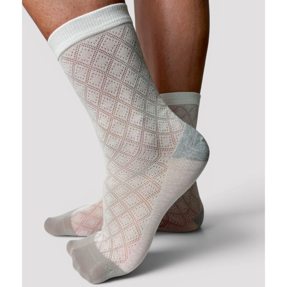 A pair of crew socks worn on a person's feet, featuring a white knit body with a subtle diamond lattice pattern and beige toe and grey heel sections, set against a plain light grey background.