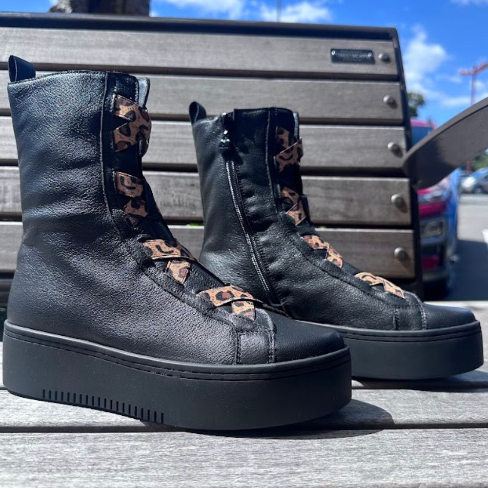 Black leather platform boots with leopard print detailing on a wooden bench.
