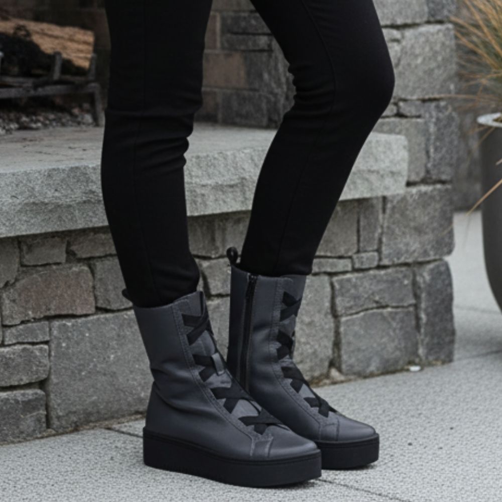 Person wearing grey boots with black soles against a stone wall background