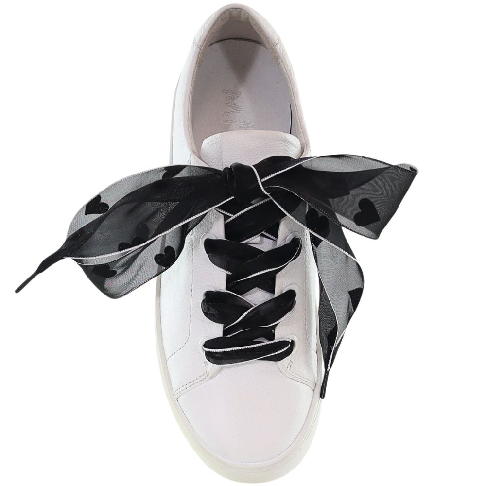 White sneaker with black decorative laces with heart motifs on a white background