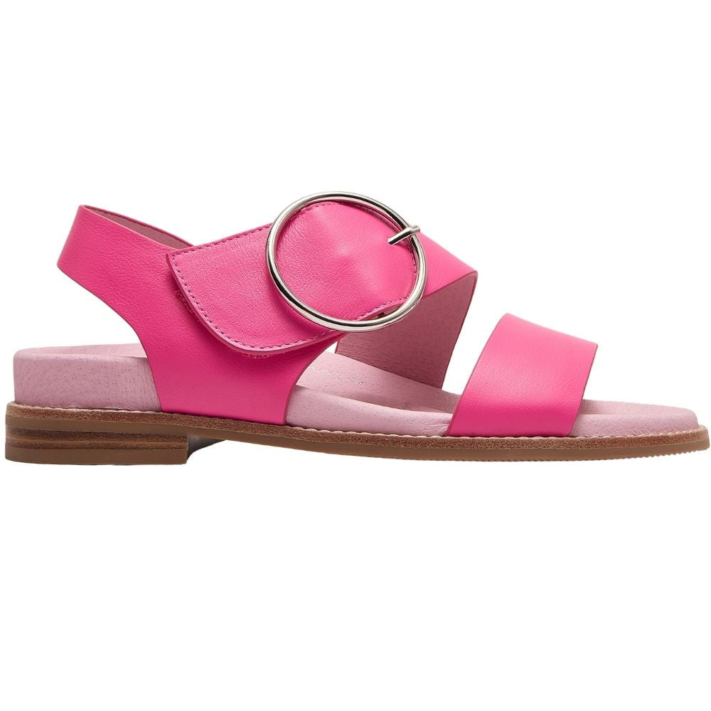 A bright pink flat sandal with two wide straps, a slingback strap, and a large round silver-tone metal ring on the top, shown in a side profile against a white background.