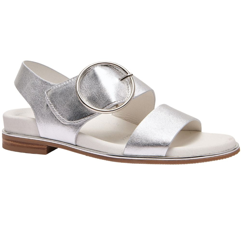 A single metallic silver flat sandal with a wide strap, a large circular silver buckle detail, and a low brown block heel, shown against a plain white background.
