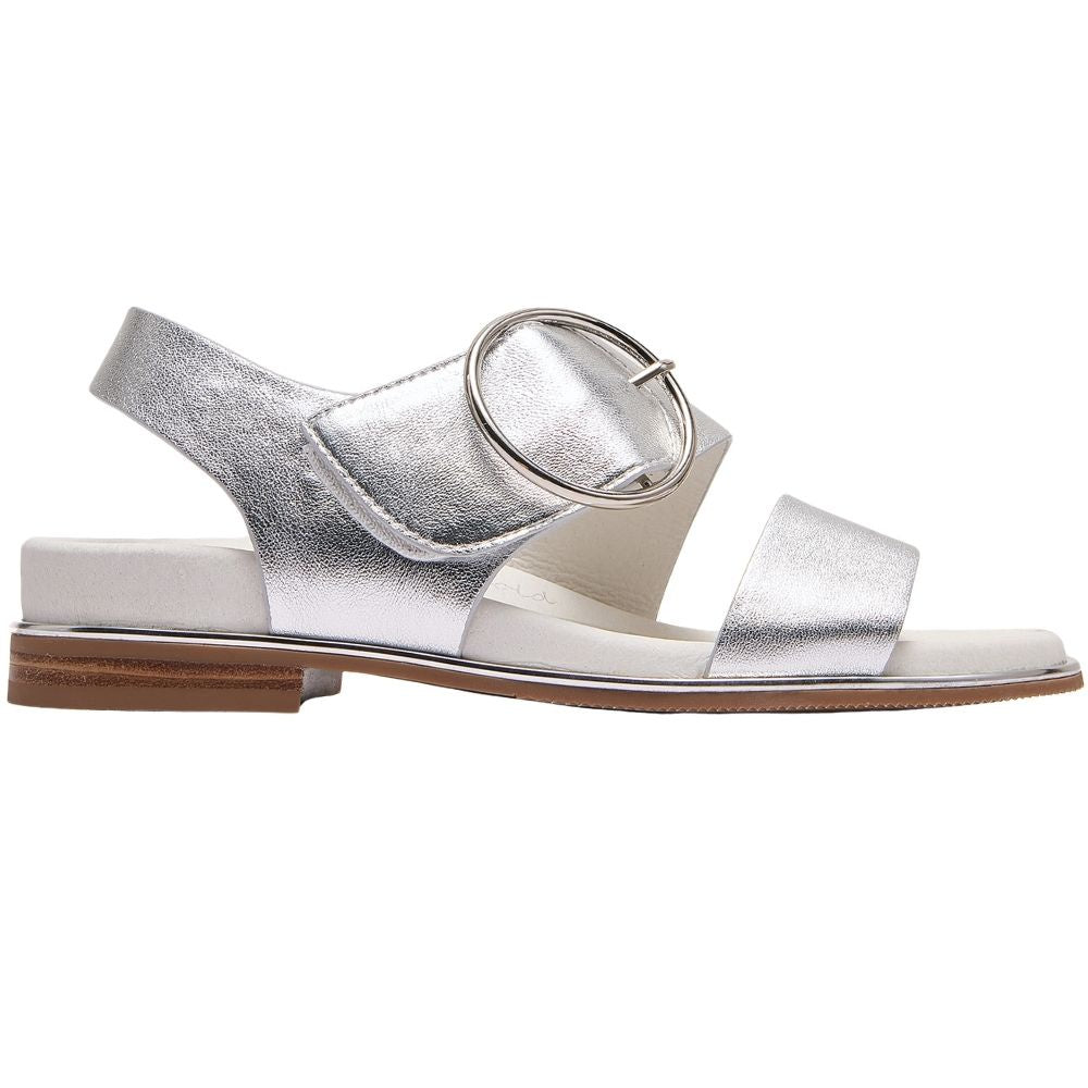 A single metallic silver flat sandal with a low brown block heel, featuring a wide front strap, a slingback strap with a large round silver buckle, and a white footbed.