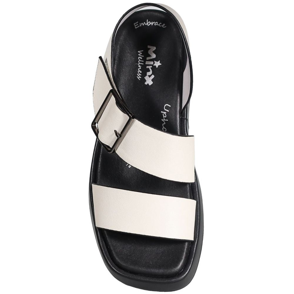 A single black and off-white leather slide sandal with a wide buckle strap, shown from a top-down view on a white background. The insole features the 'Minx Wellness' brand logo.