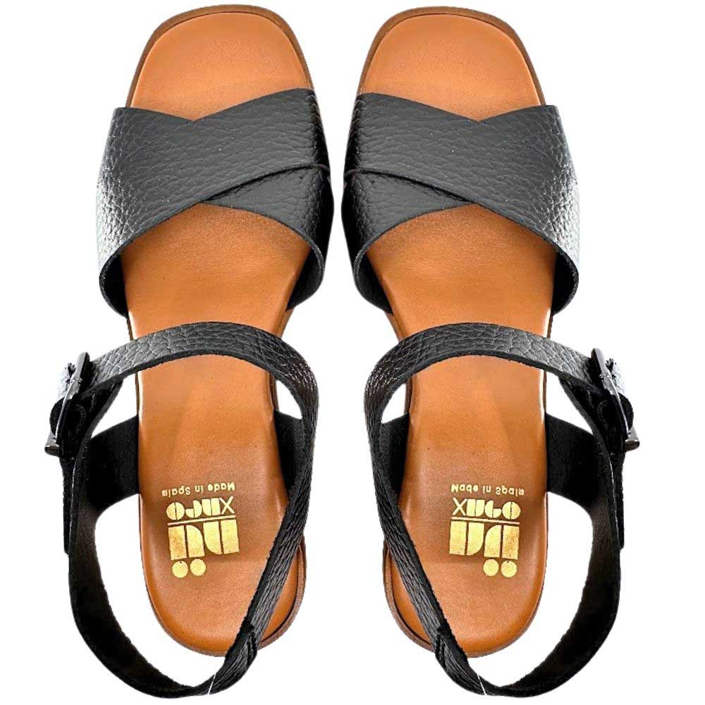A pair of black pebbled leather sandals with crisscross straps and adjustable ankle straps, shown from a top-down view on a white background. The tan footbeds feature a gold foil logo that reads 'Nu X Neo MADE IN SPAIN'.