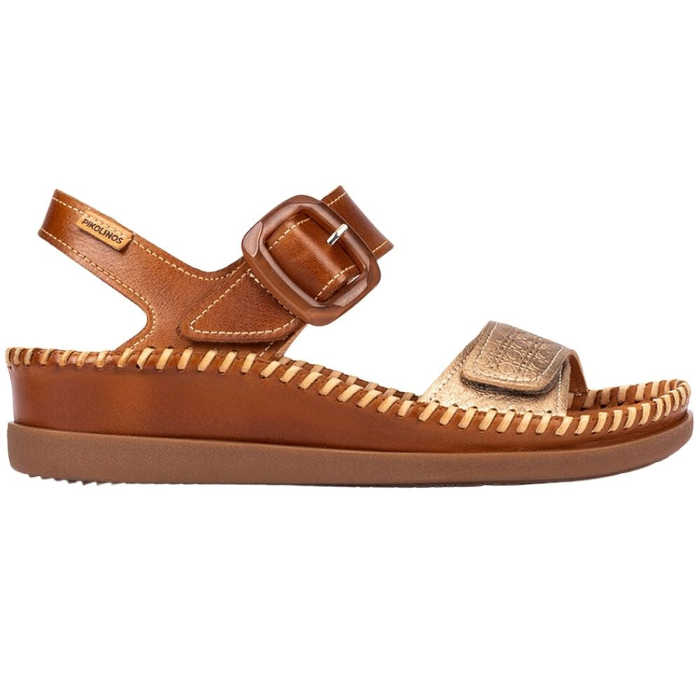 A single brown and gold leather sandal with a buckle strap, a woven rand trim detail, and a thick brown sole, shown from a side profile view on a white background.