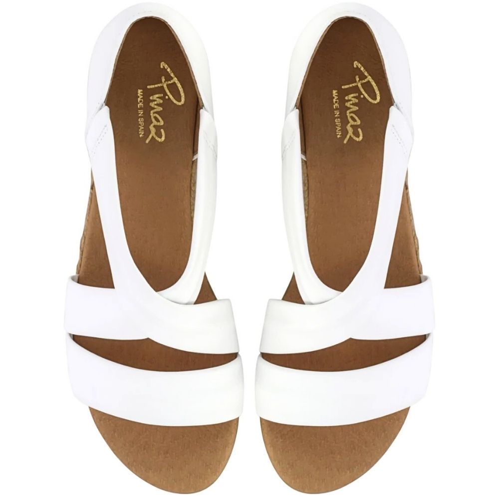 A pair of white strappy wedge sandals with tan insoles, shown from a top-down view on a white background. The brand name 'Pinaz' is printed in gold on the insoles.
