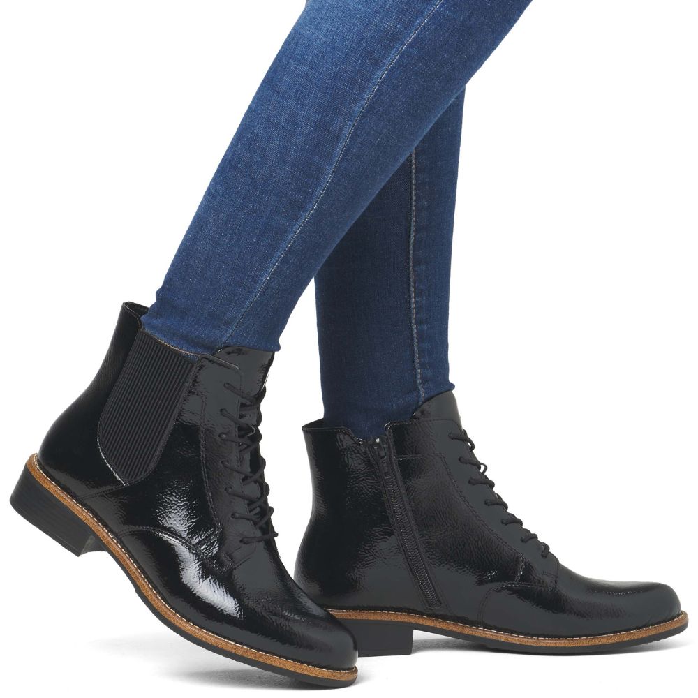 Black patent leather boots worn with blue jeans on a white background