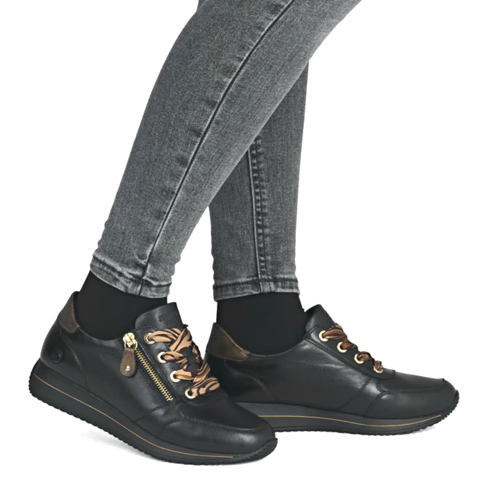 Black leather shoes with gold zippers and striped laces worn with gray jeans on a white background
