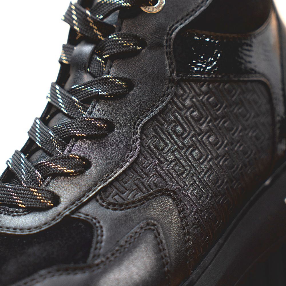Close-up of a black sneaker with textured leather and laces with gold detailing.